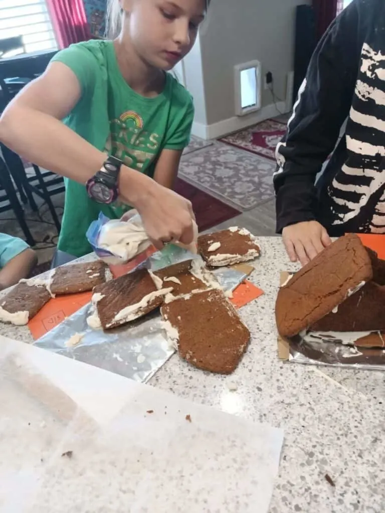 Gingerbread Nativity Instructions | Simple STEM Activity 5 little girl using a bag of royal icing to make a gingerbread nativity