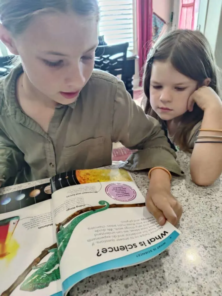 BookShark | A Science Curriculum with Engaging, Hands-on Experiments 3 two homeschooled girls reading a bright and colorful BookShark science book