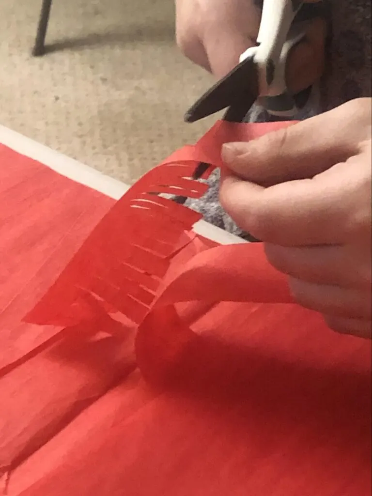 Paper Mache Dragon STEM and Craft Project Tutorial 14 scissors cutting fringes onto red tissue paper strips for dragon paper mache project